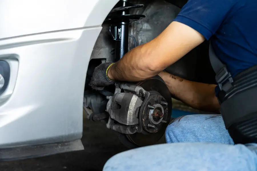 Mechanic crouched beside a vehicle's wheel, working on the brake hub area.